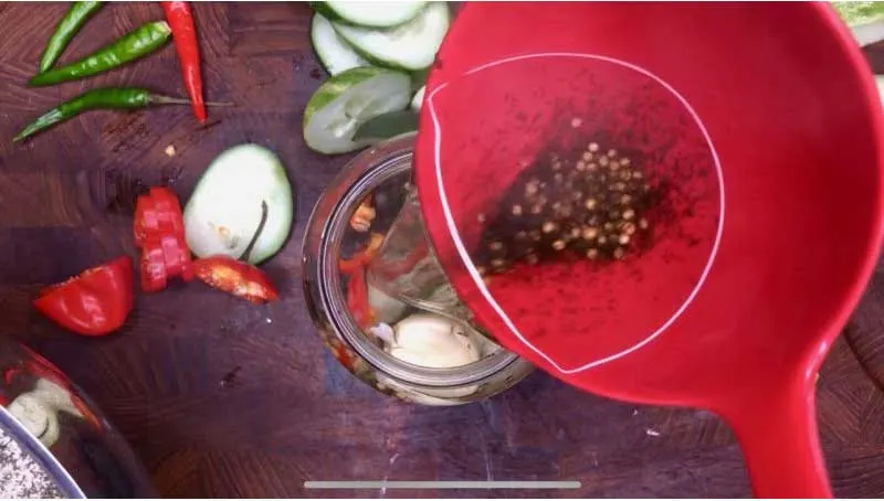 Pouring brine into jar with cucumbers and peppers