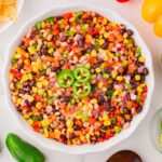 Overhead shot of Texas caviar in a bowl surrounded by ingredients like peppers, lime and tortilla chips for dipping