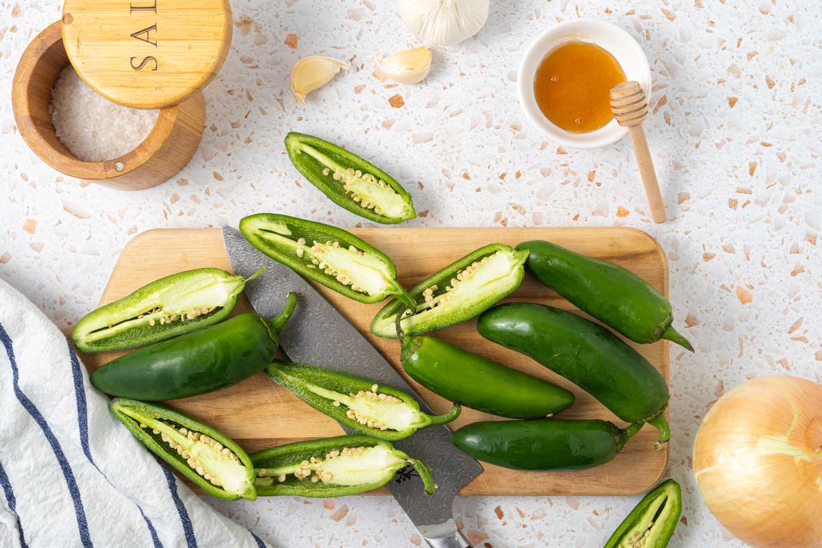 Sliced peppers on a cutting board with knife, honey and garlic cloves