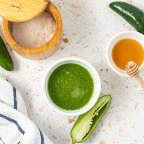 Overhead shot of jalapeno hot sauce in a serving bowl with honey and fresh peppers