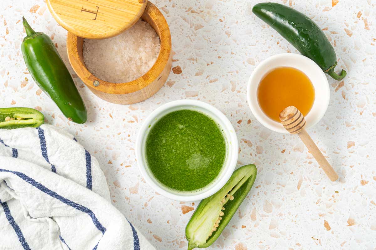 Overhead shot of jalapeno hot sauce in a serving bowl with honey and fresh peppers
