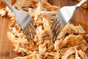 Chicken being shredded on cutting board
