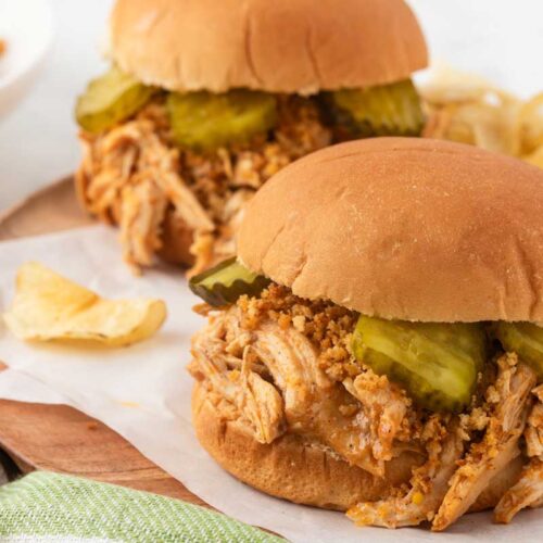 slow cooker nashville chicken on a bun, surrounded by chips and pickles peeking out